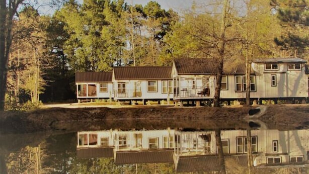 A row of cabins with a reflective water body in the foreground, surrounded by trees.