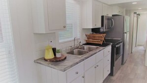 A modern kitchen with white cabinetry, a granite countertop, a microwave, and a stainless steel refrigerator.