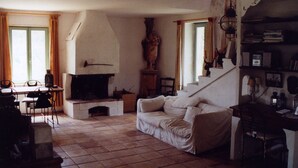 Een woonkamer met een open haard, een bank, een eettafel met stoelen en een trap.