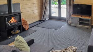 A cozy living room with a wood-burning stove, grey sofa, and a flat-screen TV on a wooden stand. - 2 bedroom accommodation in Ulrome (Ulrome)