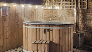 A wooden hot tub with a metal frame, a small wooden bench, and a brick wall in the background. - 2 bedroom accommodation in Ulrome (Ulrome)