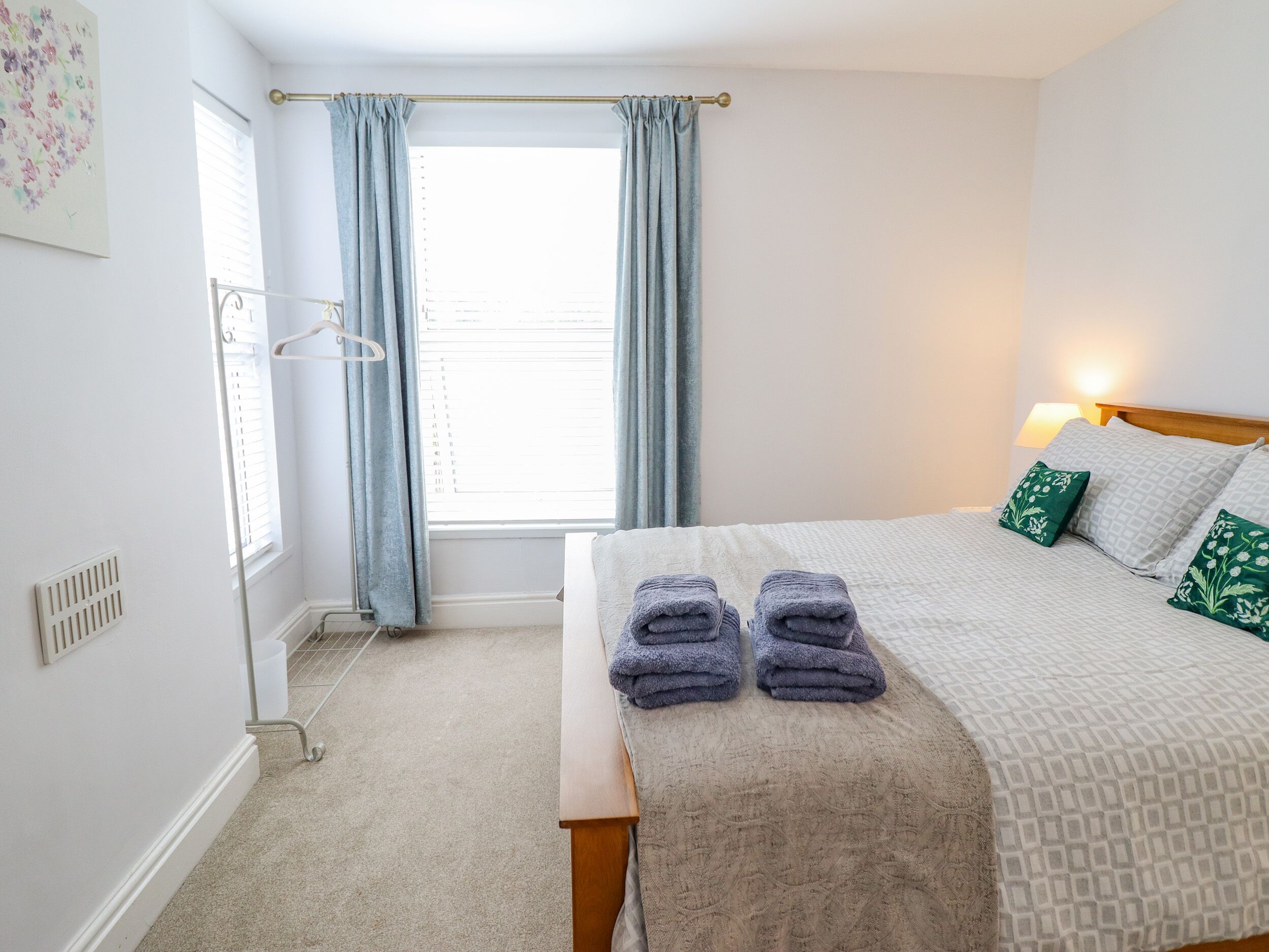 Quarto com cama, mesa de cabeceira, abajur e janela com cortinas.