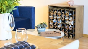 Una habitación acogedora con un sofá azul, una estantería de madera para vino, una pequeña planta en maceta y una mesa con un cuaderno y un bolígrafo.