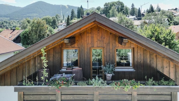 Una cabaña de madera con techo a dos aguas, ventanas amplias y un balcón con plantas.