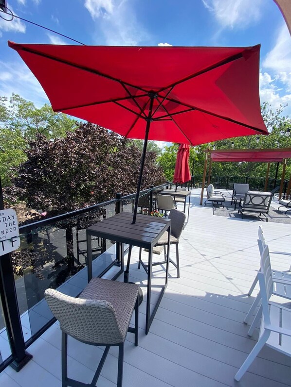 An outdoor patio with tables and chairs, a red umbrella, and a sign on the glass door. - Rooftop patio Hot Tub/ 2 BBQ/ firepit/Full Games room/7 Beds/5 floors (Grand Bend)