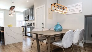 A modern kitchen with a wooden dining table, grey upholstered chairs, and a blue vase centerpiece.