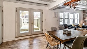 A dining area with a wooden table and chairs, a sofa with cushions, and a view of the backyard through glass doors.