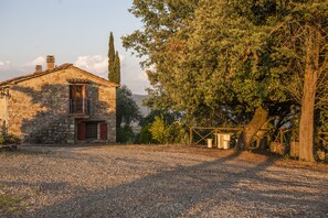 Un bâtiment en pierre doté d’un balcon, entouré d’arbres et bordé d’un chemin de gravier.
