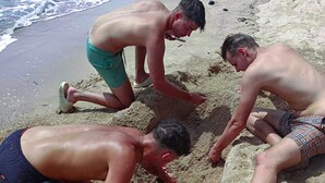 Drie mensen op een zandstrand, bezig met een activiteit.