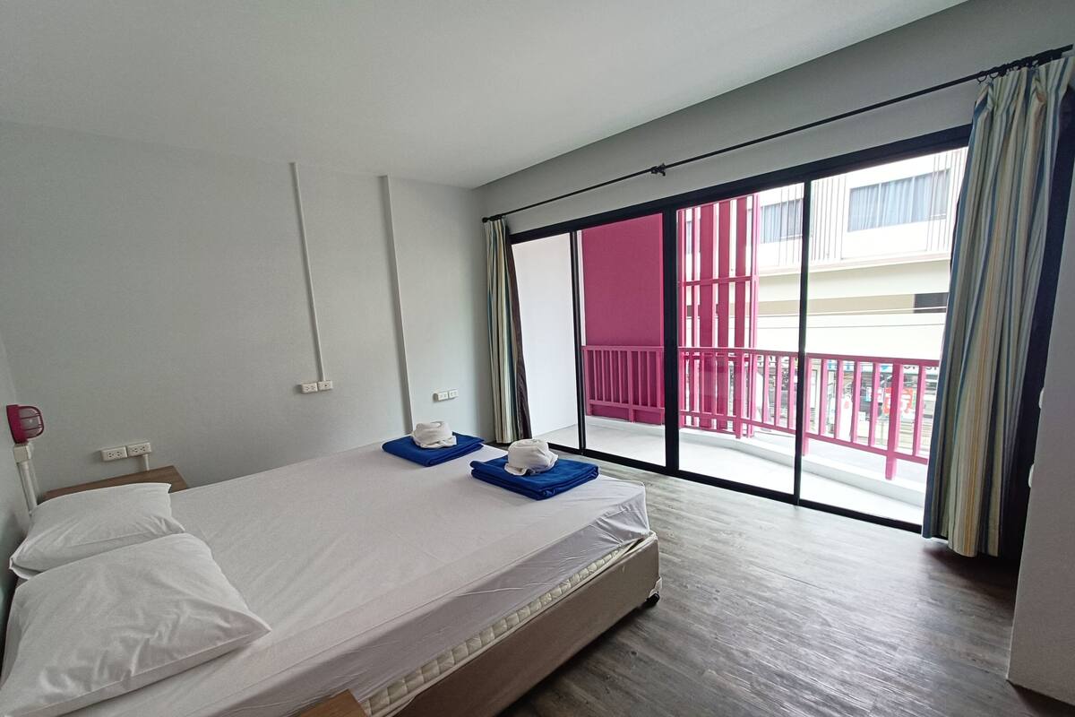 A hotel room with a bed, a window with a view of a balcony, and a door leading to the balcony.