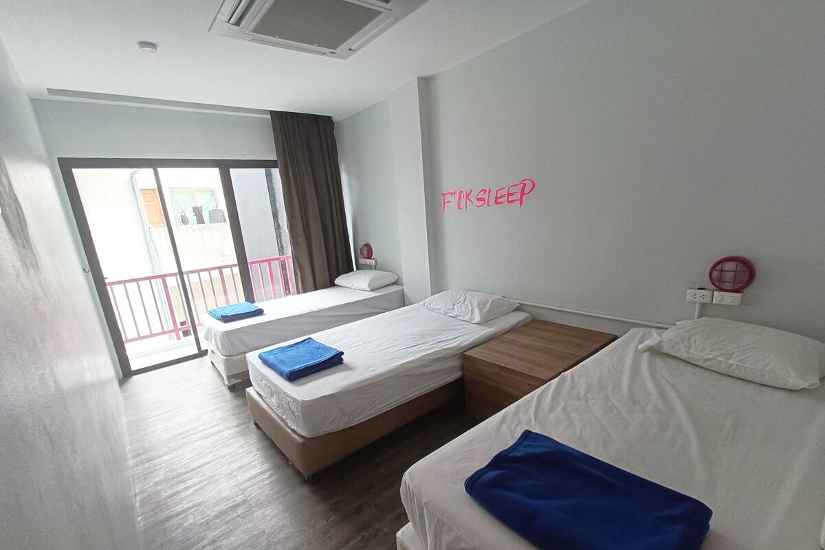 A hotel room with two single beds, a large window with a view, and a sliding door leading to an outdoor balcony.