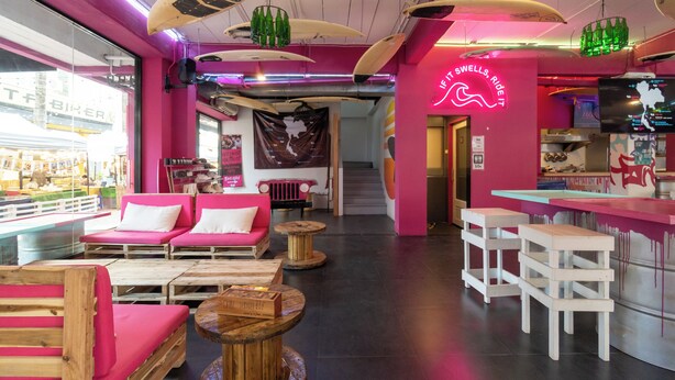 Een levendige bar met surfplanken aan het plafond, een neonbord en een toog.
