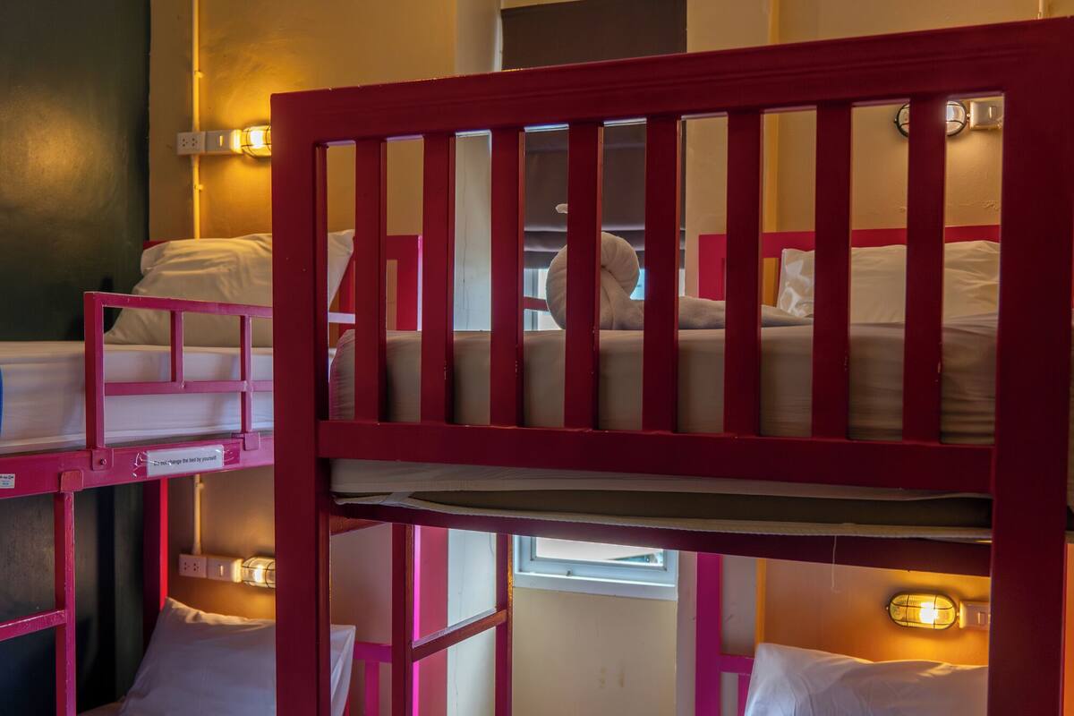 A dormitory-style room with bunk beds, each with a pillow and a blanket.