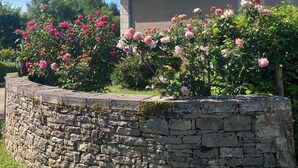 Un muro de piedra con un jardín de rosas rosadas frente a un edificio con una chimenea.