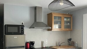 Una cocina compacta con microondas integrado, un refrigerador de acero inoxidable, armarios de madera, un lavamanos y una mesa de comedor con una silla.