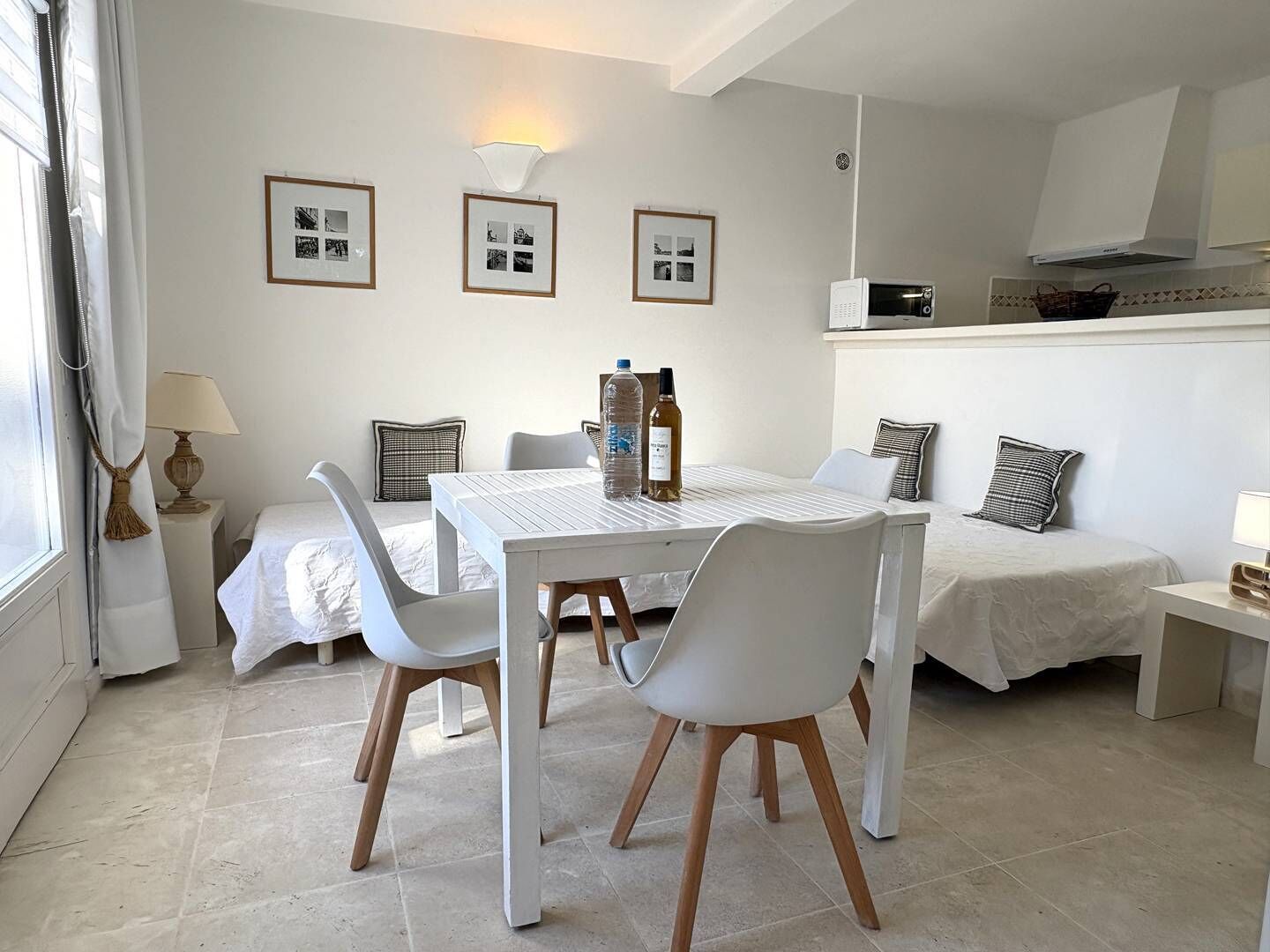 A modern, well-lit room with a dining table, chairs, a sofa, and a bed. There are framed pictures on the wall, a lamp, and a microwave.