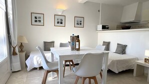 Une pièce moderne et bien éclairée, comprenant une table à manger, des chaises, un canapé et un lit. On y trouve également des tableaux encadrés au mur, une lampe et un four à micro-ondes.
