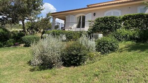 Une maison dotée d’un porche abrité, de volets blancs et d’un jardin où poussent différentes plantes, ainsi qu’une pelouse.