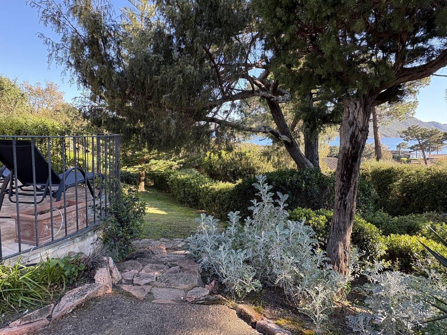 A garden with a paved path, a metal fence, and a seating area with chairs.