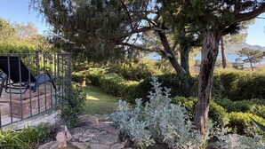 Un jardin avec un chemin dallé, une clôture en métal et un espace aménagé avec des chaises.