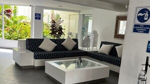 A modern waiting area with a sofa and a glass-top coffee table, a sign indicating hand sanitizer availability, and a view of greenery outside. - Stunning 3 Bedrooms Apartment in San Andres (San Andrés)