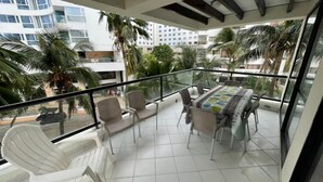 A balcony with white chairs, a dining table with a patterned tablecloth, and a view of palm trees and buildings. - Stunning 3 Bedrooms Apartment in San Andres (San Andrés)