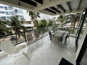 Un balcon avec une table et des chaises, entouré de palmiers et offrant une vue sur d’autres immeubles.