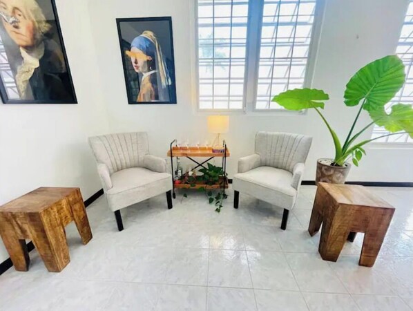 Une pièce avec deux fauteuils placés face à face, une petite table avec une lampe et une grande plante en pot.