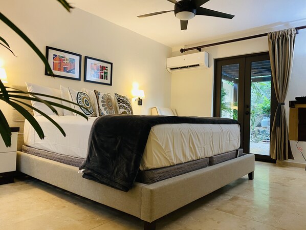 Un dormitorio con cama, ventilador de techo, aire acondicionado, ventana con cortinas y una lámpara de pared.