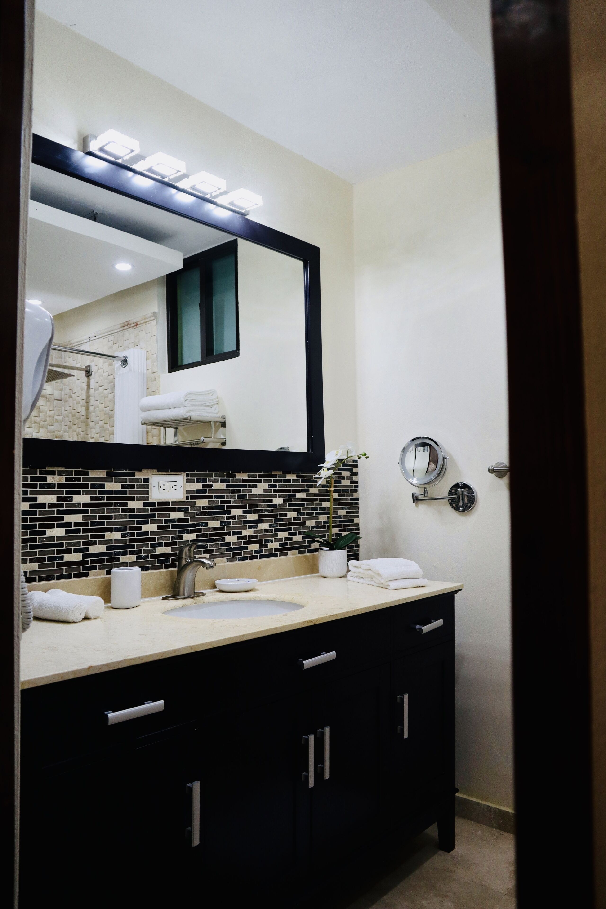 A bathroom with a black and white tiled backsplash, a sink with a mirror above it, and a towel rack.