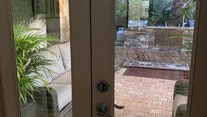 Eine Glastür führt zu einer Terrasse mit Steinwand, Grill und Topfpflanzen.