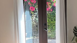 Ein Zimmer mit einem Bett, einer Schiebetür zu einem Außenbereich mit rosa Blumen und einem Blumentopf.