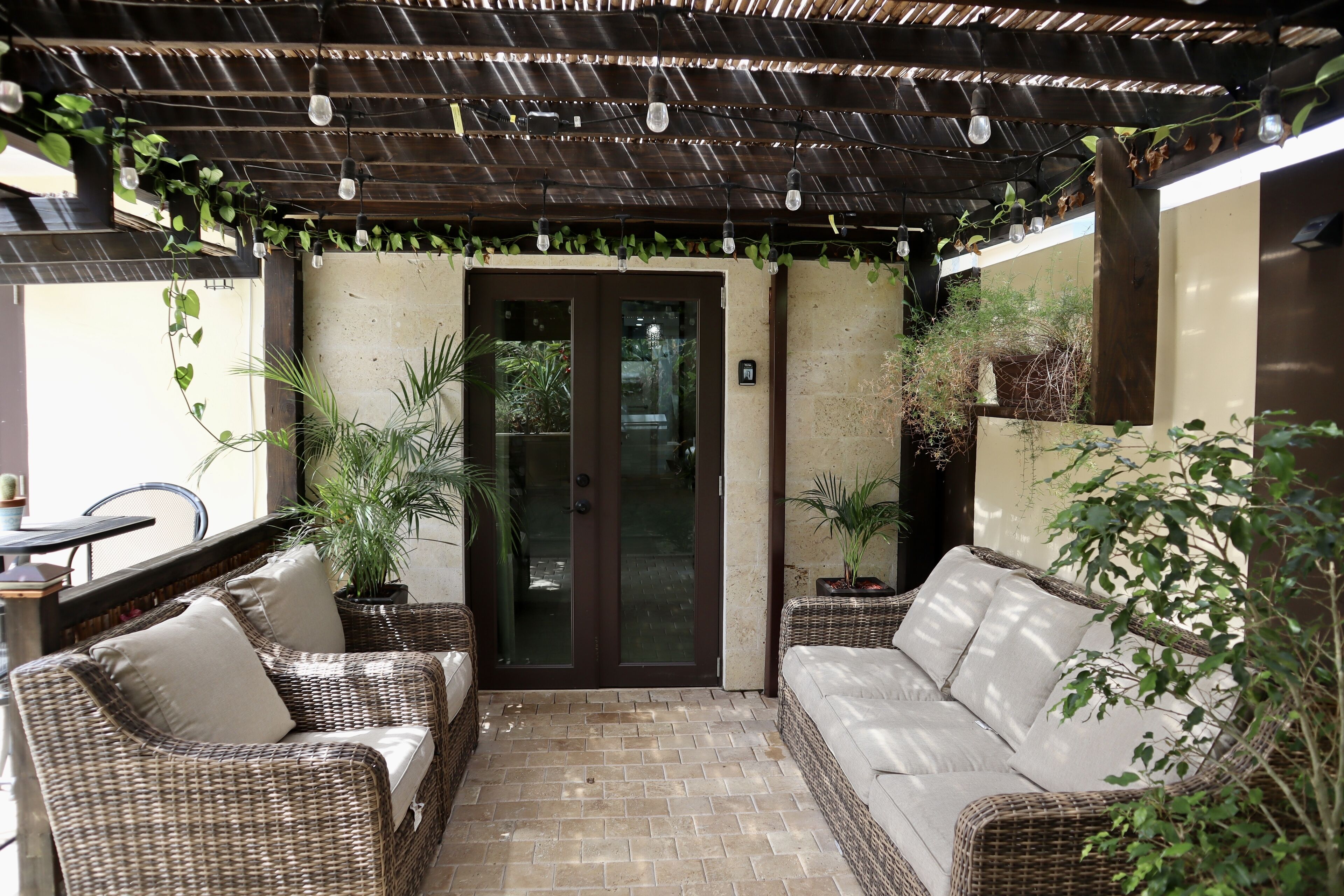 Ein überdachter Patio-Bereich mit Korbmöbeln und Kübelpflanzen.