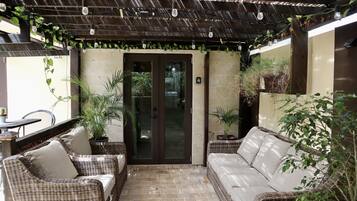 Ein überdachter Patio-Bereich mit Korbmöbeln und Kübelpflanzen.