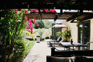 Un patio con mesa y sillas, rodeado de abundante vegetación y plantas florecientes.
