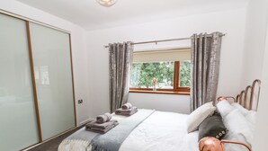 A bedroom with a bed, a window with curtains, a bedside table, and a view of greenery outside. - Awel-y-mor (Caernarfon)