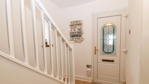 A staircase with a white railing leading to a door with a glass panel. A sign on the wall reads "A LITTLE SAND BETWEEN THE TOES ALWAYS TAKES AWAY THE WOES." - Awel-y-mor (Caernarfon)