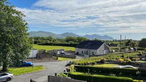 A rural house with a paved driveway, a fenced yard, and a car parked in the foreground. - Awel-y-mor (Caernarfon)