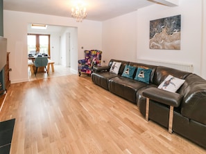 Una sala moderna con un sofá de cuero, un sillón colorido y una zona de comedor con muebles de madera.