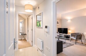A modern apartment with a hallway leading to a living area, a TV, and a seating area. - Roomspace Apartments - Lomond Court (Surbiton)