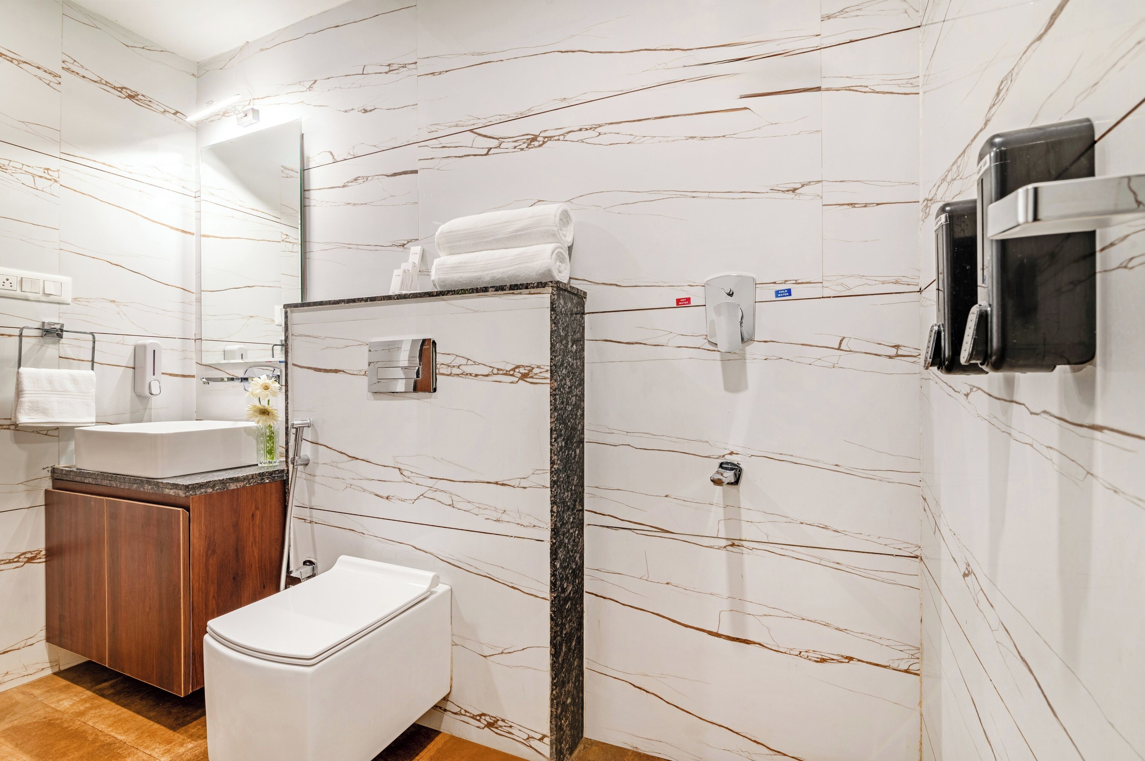 A modern bathroom with a marble backsplash, a wooden vanity, a white toilet, and a towel rack.