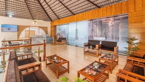 A spacious lobby with wooden furniture, a glass wall with a cityscape view, and a ceiling with a metal grid pattern. - Sterling Banashree Badami  (Badami)