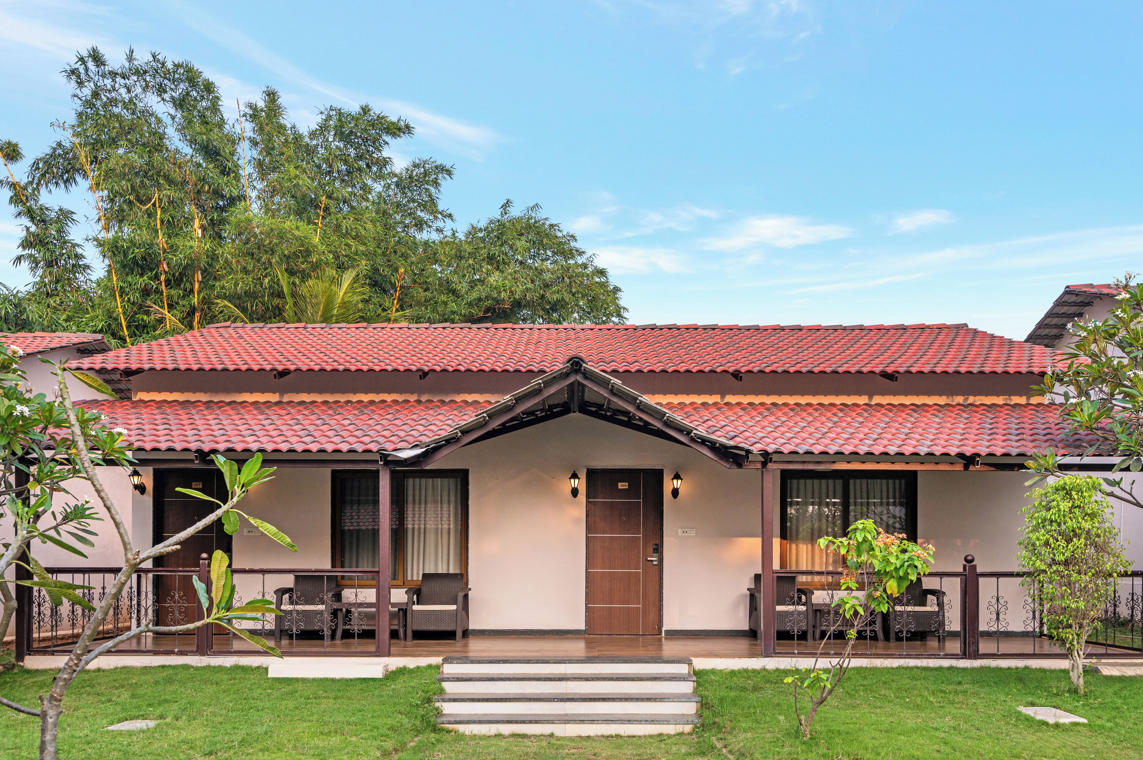 A two-story building with a red-tiled roof, a front porch with a bench, and a small garden area.