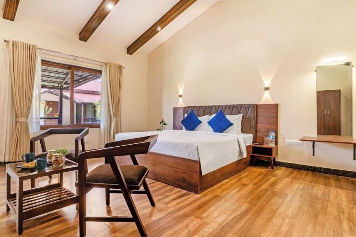 Un dormitorio con una cama de madera, dos mesitas de noche, una silla, una pequeña mesa con una planta y una ventana con cortinas.