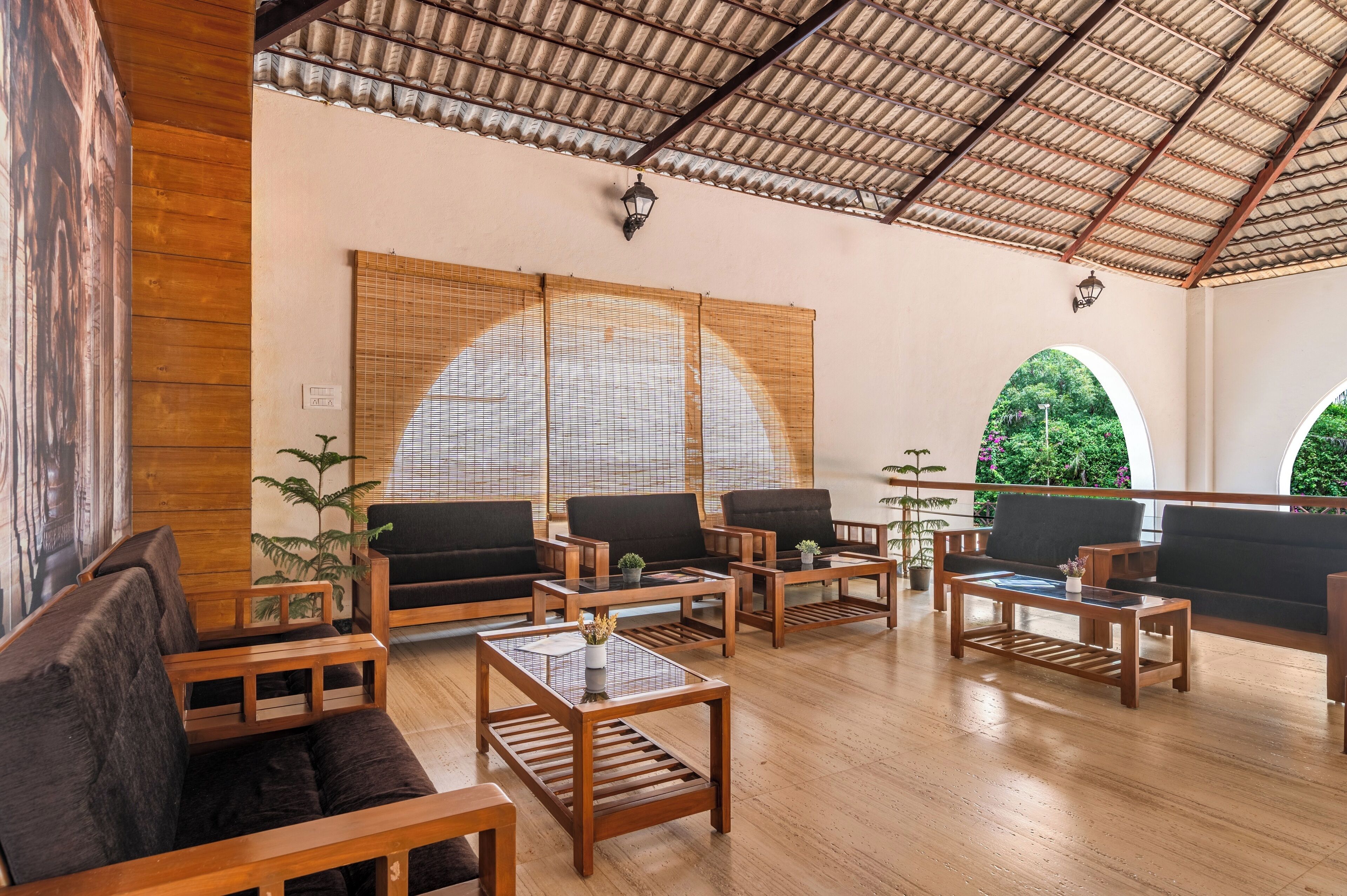 Amplio espacio interior con mobiliario de madera, incluyendo sofás y mesas, y grandes ventanales con persianas de bambú.