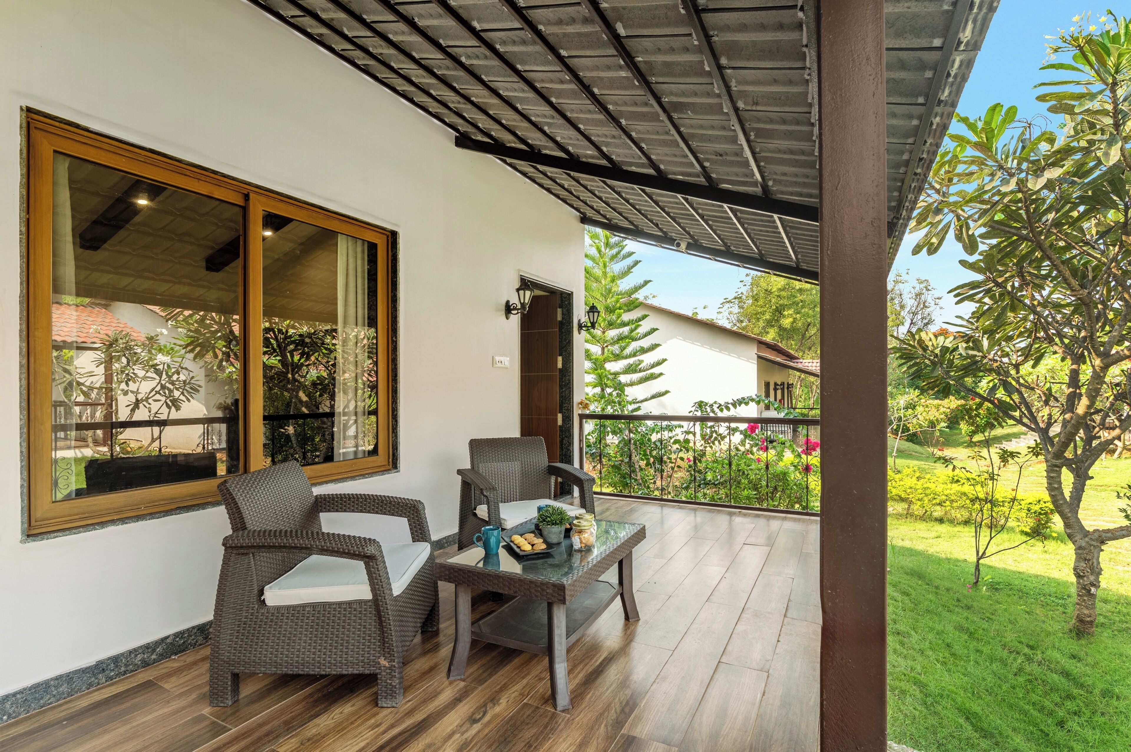 A covered patio with wicker furniture, a glass table, and a view of a garden.