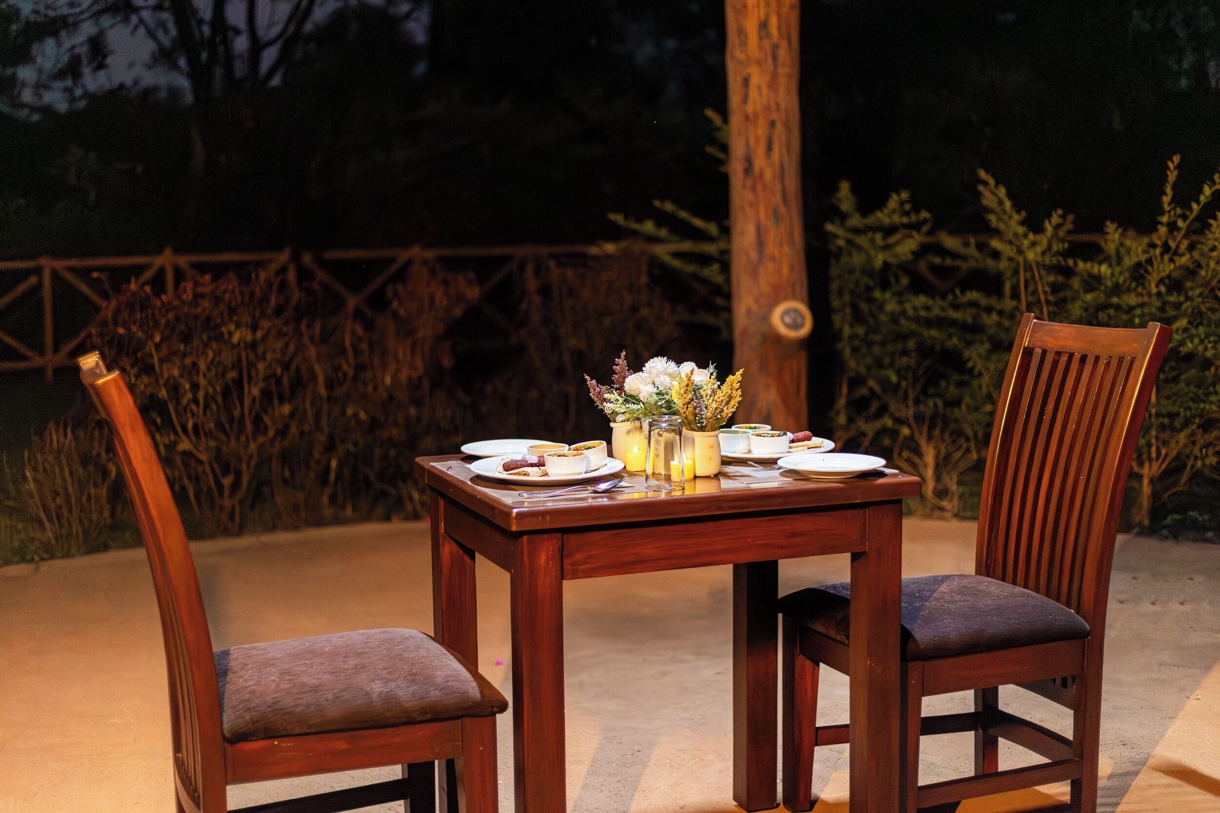 An outdoor dining table with chairs, plates, and a vase of flowers.