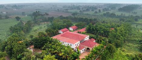 A large building with a red roof surrounded by lush greenery and fields.