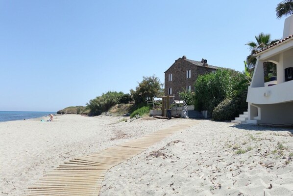 A beach with a wooden boardwalk leading to a stone building with a garden.