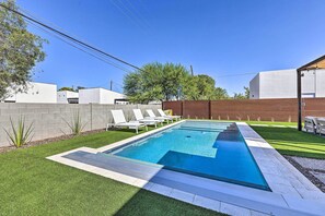 A rectangular swimming pool with a clear blue water surface, surrounded by a well-maintained lawn and a low brick wall. - Backyard Oasis w/ Pool! Family Getaway in Phoenix (Phoenix)